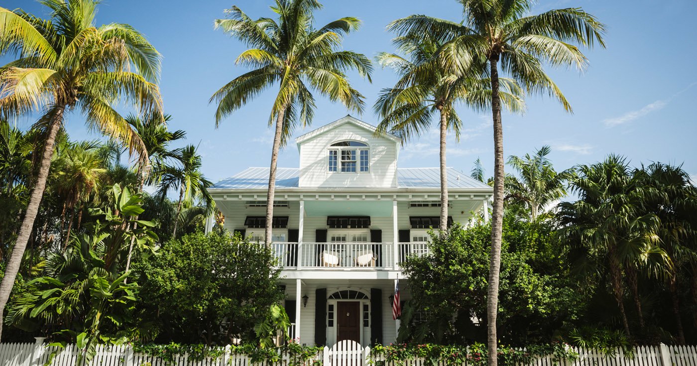 Large White Home with Black Shutters Surrounded by a Tropical Imperial Palms and a White Picket Fence
