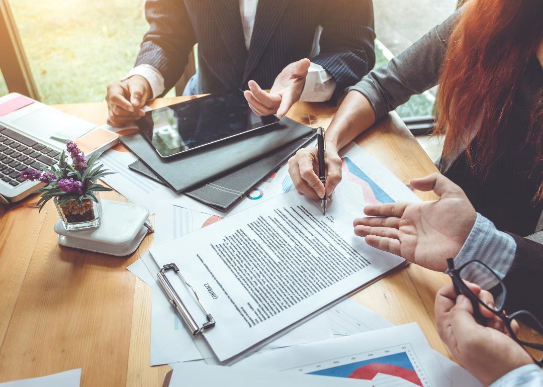 “Photograph of three people discussing and signing paperwork” - Source: Canva