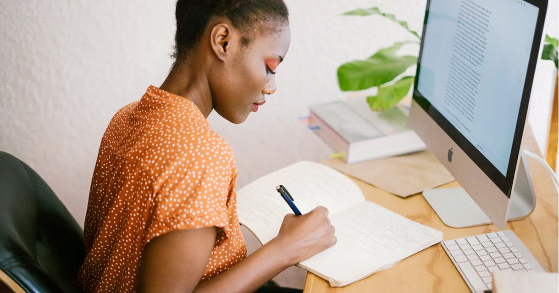 "Woman in Orange Writing in Notebook on Wooden Desk