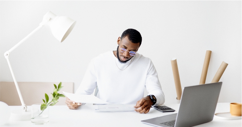 Person in Reviewing Documents on White Desk with Laptop and White Lamp