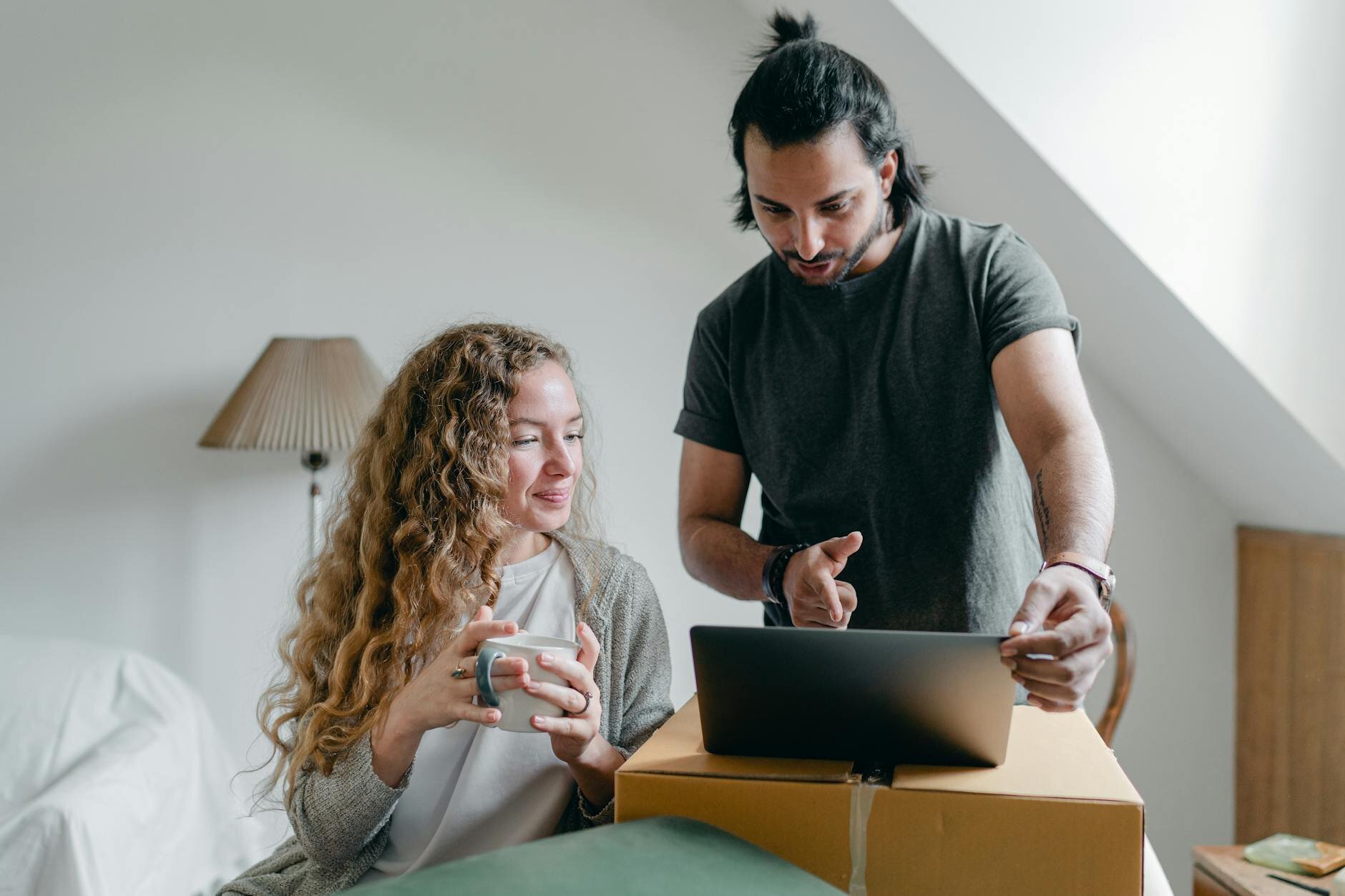 Couple sitting together in apartment, looking at a laptop with relieved expressions, researching the minimum credit score needed to qualify for a mortgage.