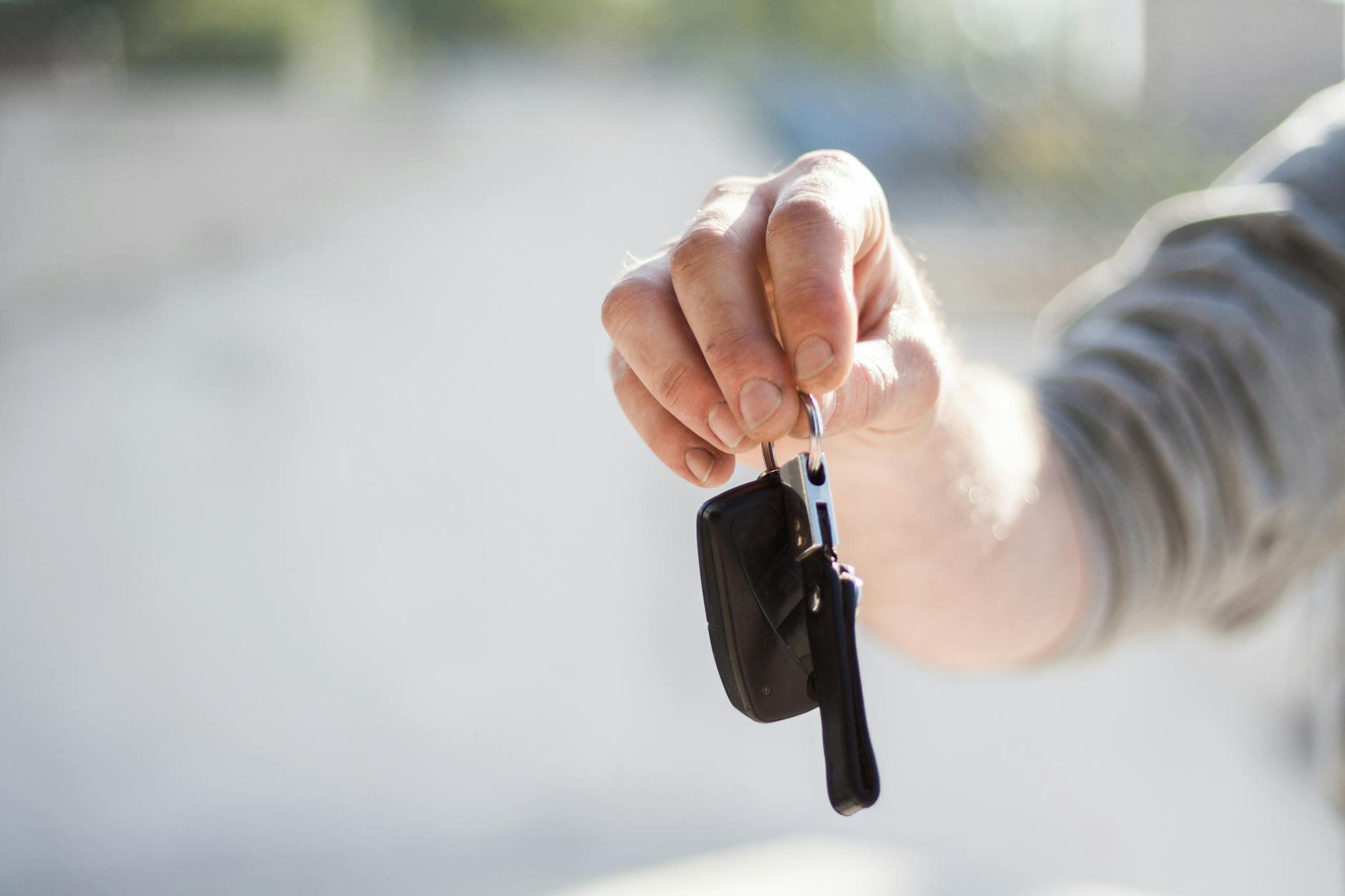 Person holding a car key fob, extending it forward as if handing over the keys.