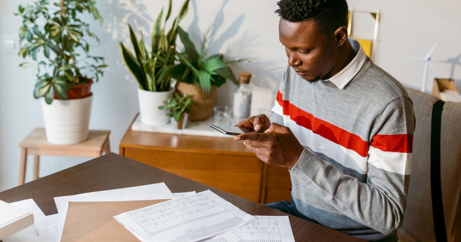 Person Sitting at Table with Scattered Paperwork Reviewing Contents on Cell Phone