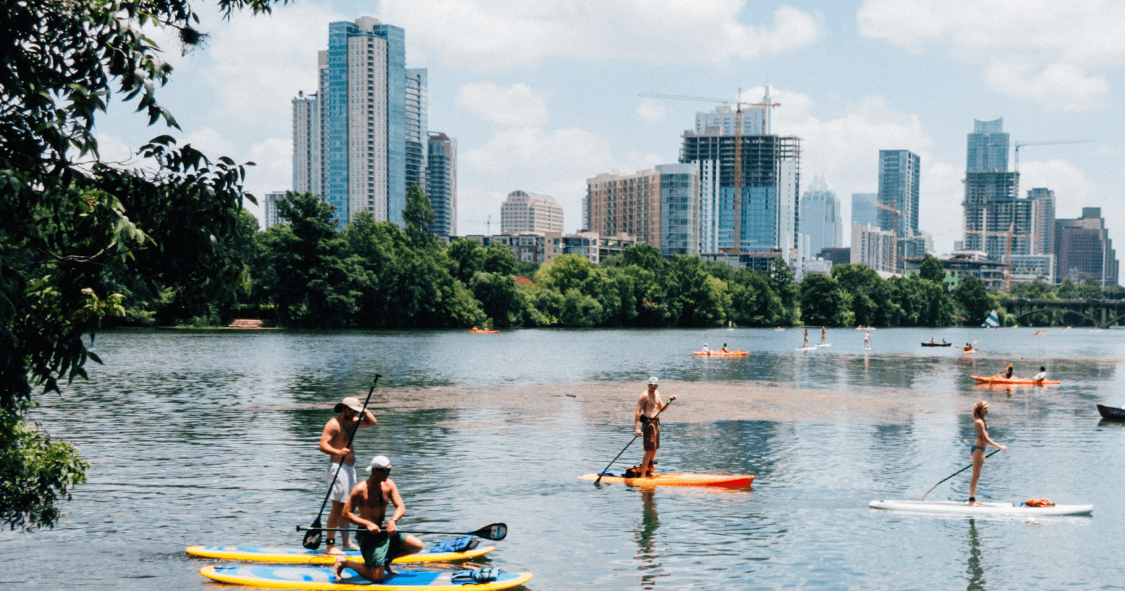 Photograph of People Paddle Boarding With Cityscape View of Austin, TX