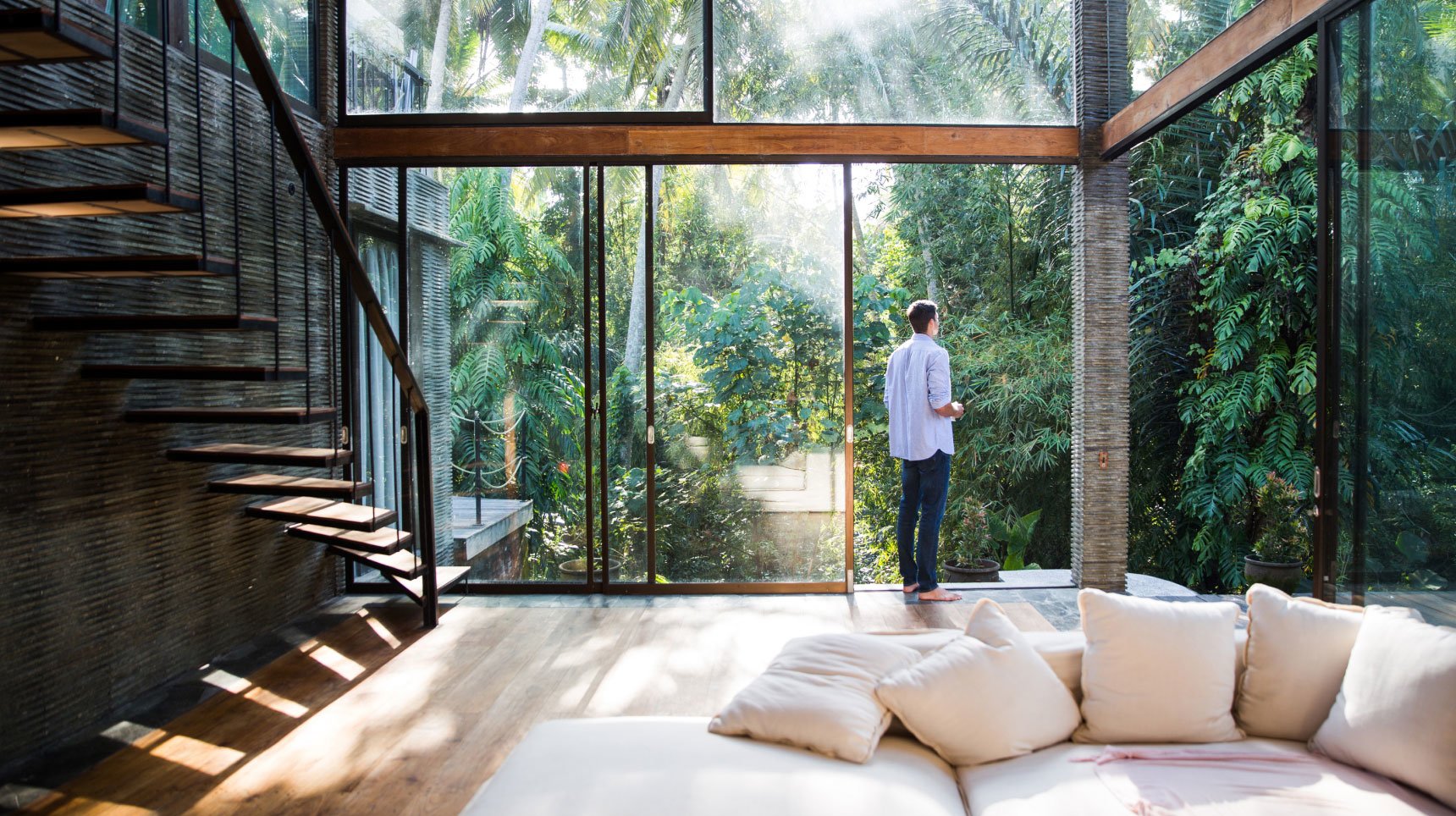 Man Stepping Outside of a Modern Floor to Ceiling Glass Home Looking at Lush Greenery
