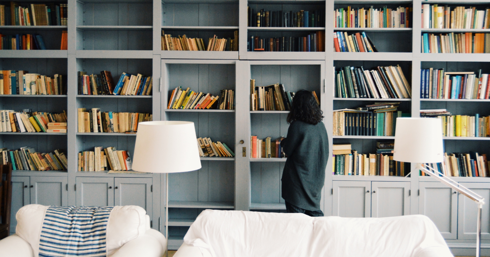 Person Standing in Front of Large Bookshelf In Living Room
