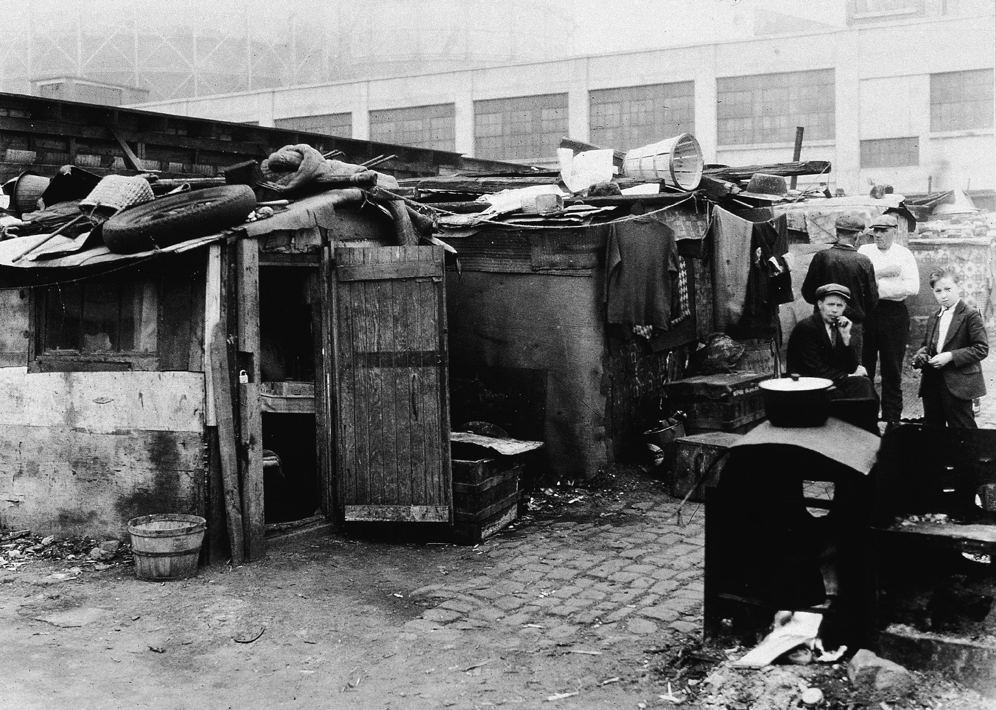 Black-and-white photograph of people standing in front of makeshift housing shacks - American Stock Archive // Getty Images