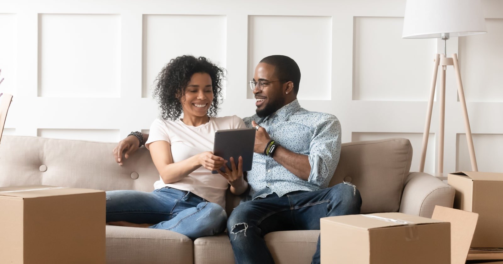 Two People Smiling and Seated Close Together on Sofa Surrounded by Moving Boxes