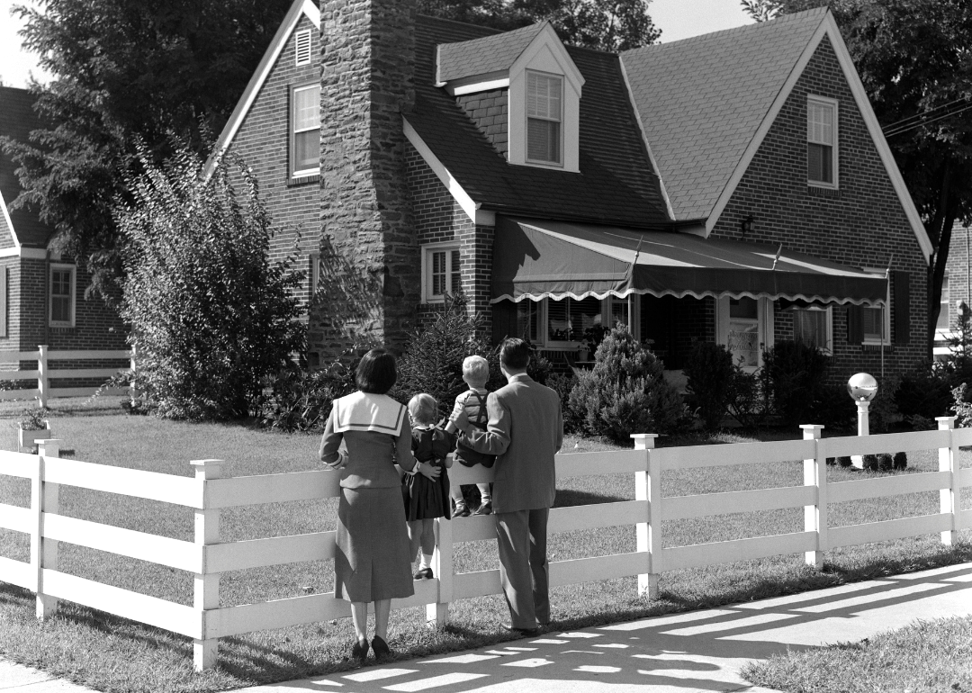 Armstrong Roberts/ClassicStock // Getty Images - 50’s era black-and-white photograph of a family of four standing outside of a home