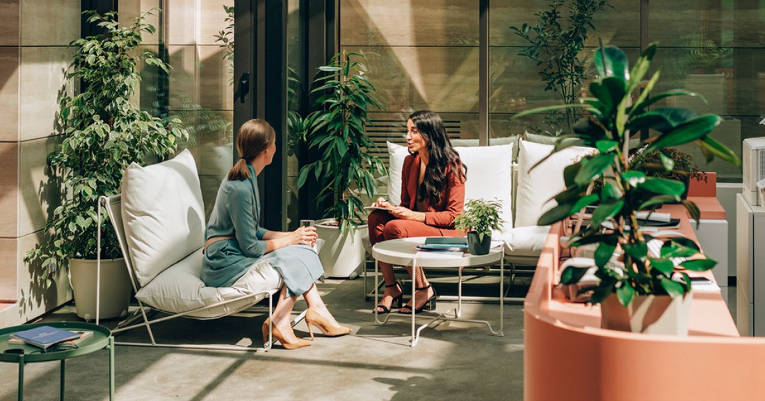 Two women talking in well lit plant filled room