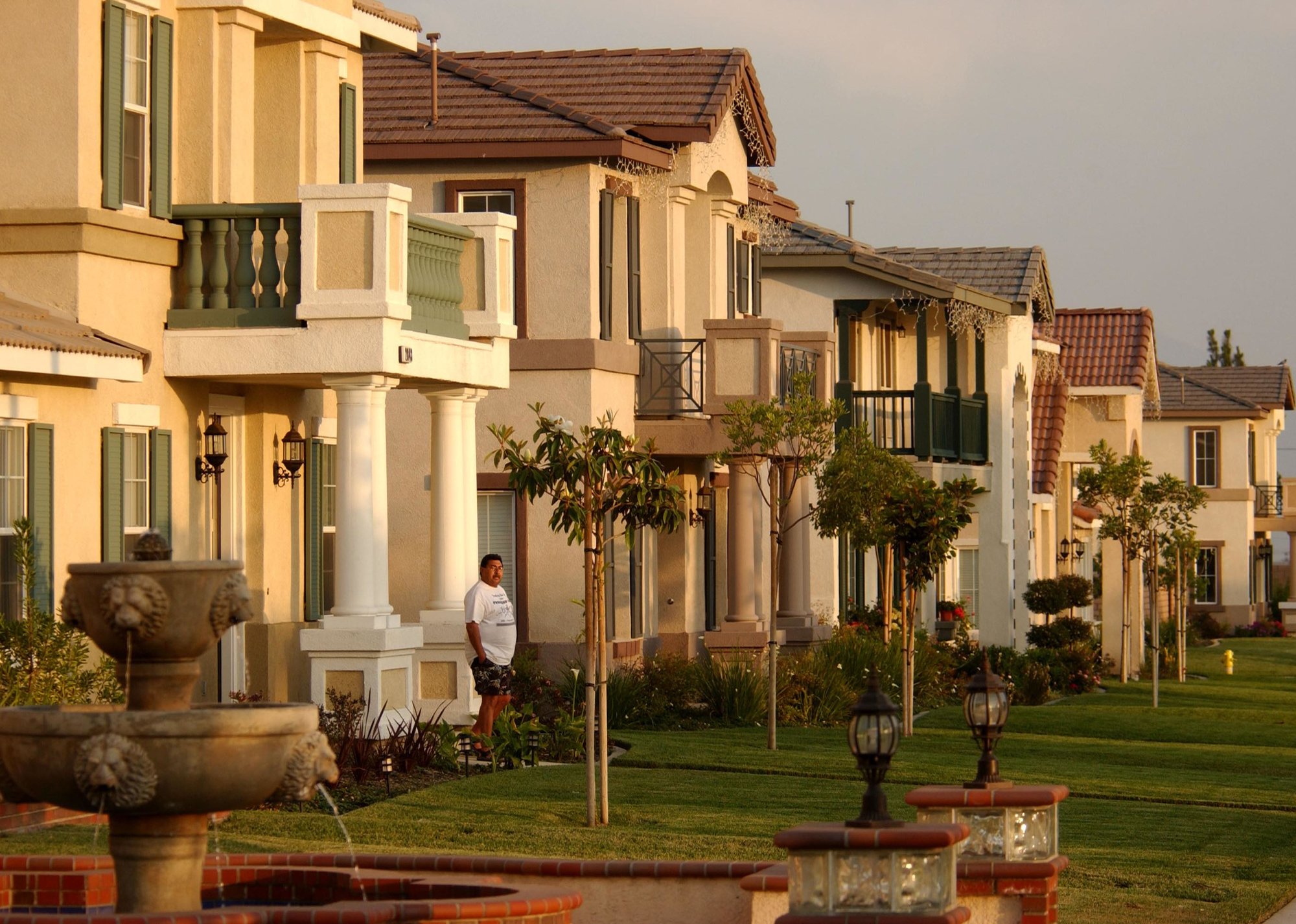 Row of two story homes with small trees outfront, small fountain in foreground - Source: David McNew // Getty Images