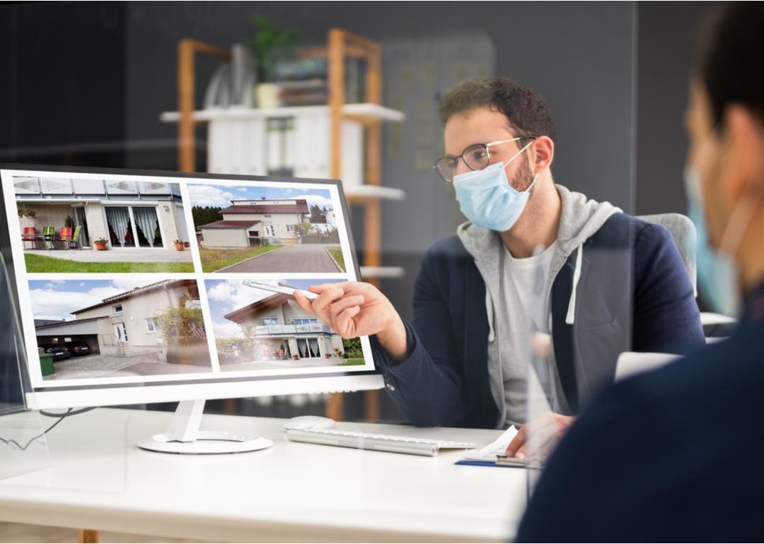 “Photograph of a mask-wearing real estate agent pointing to listings on a computer screen” - Source: Andrey_Popov // Shutterstock