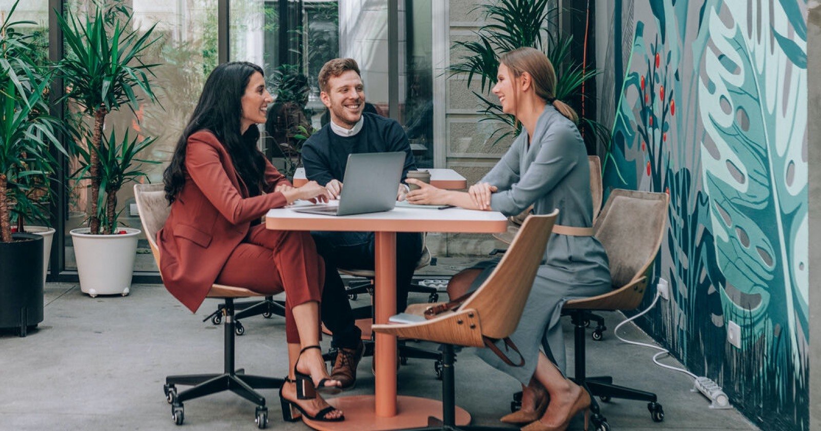 Three People Seated in Stylish Office Smiling and Having a Conversation Around a Table