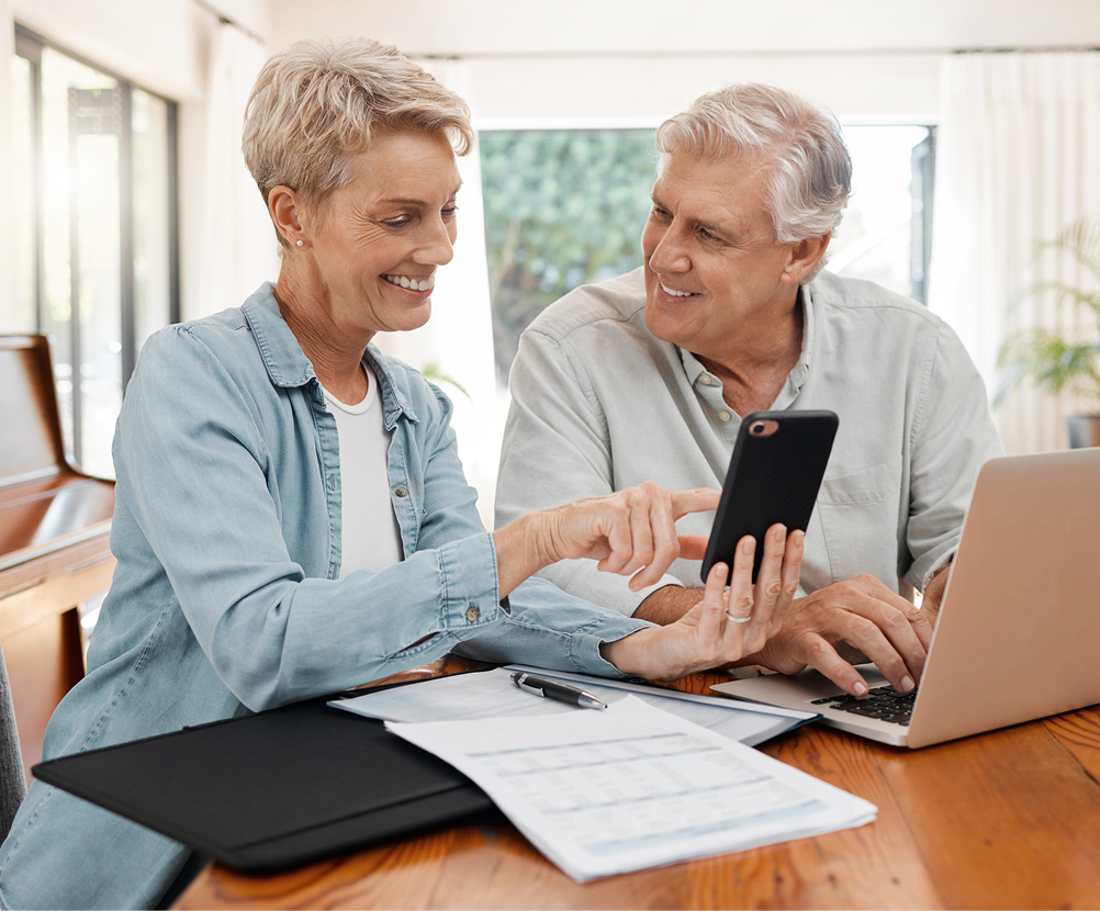 Older couple reviewing finances at home using a phone and laptop.