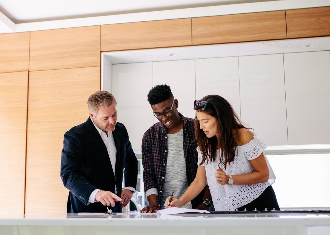 “Photograph of a couple signing mortgage paperwork, with an agent reviewing” - Source: Canva