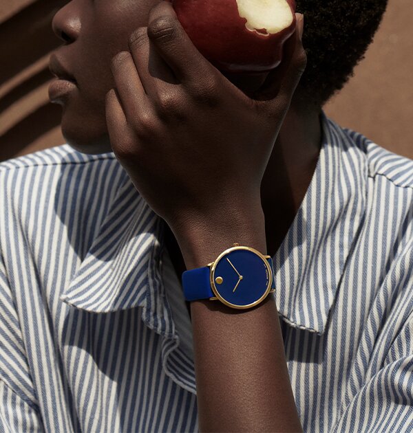 Woman wearing a blue Modern 47 watch with leather stap while holding an apple