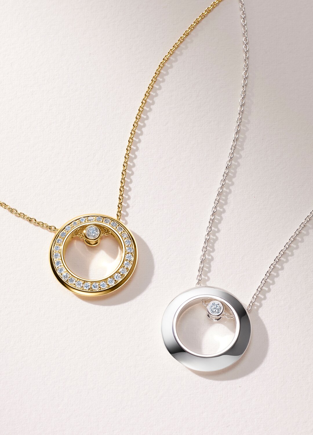 Gold tone necklace with lab grown diamonds next to a silver necklace with one lab grown diamond.