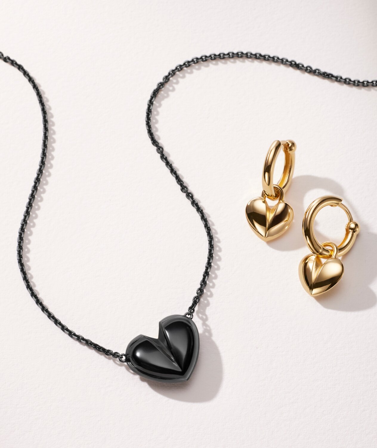 Women's black plated heart necklace next to gold tone hoop earrings with heart charm.