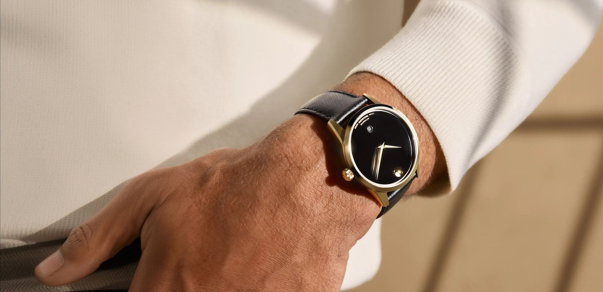 Man in a white sweater wearing the black Museum Classic automatic strap watch with gold tone accents.