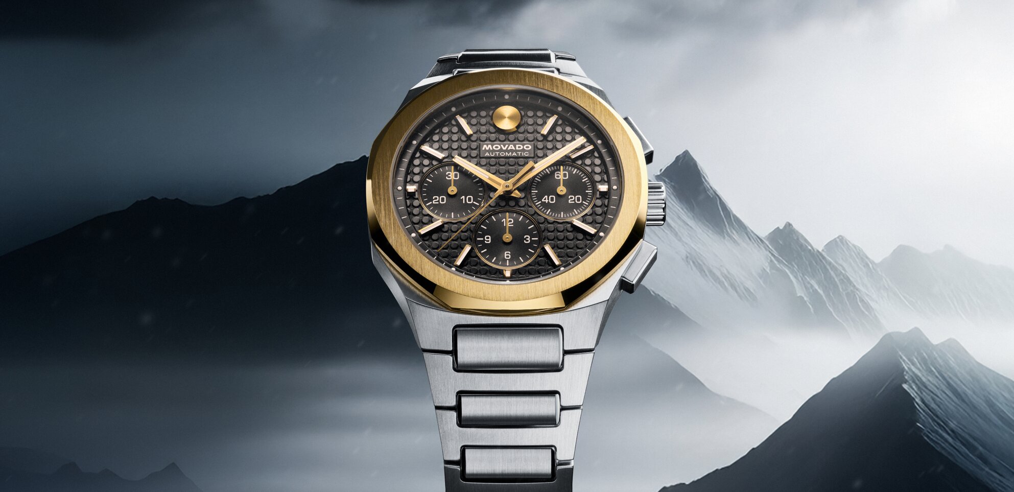 Alta Centurion Chronograph watch with stainless steel bracelet, grey dial and 18k gold bezel in front of a mountain.