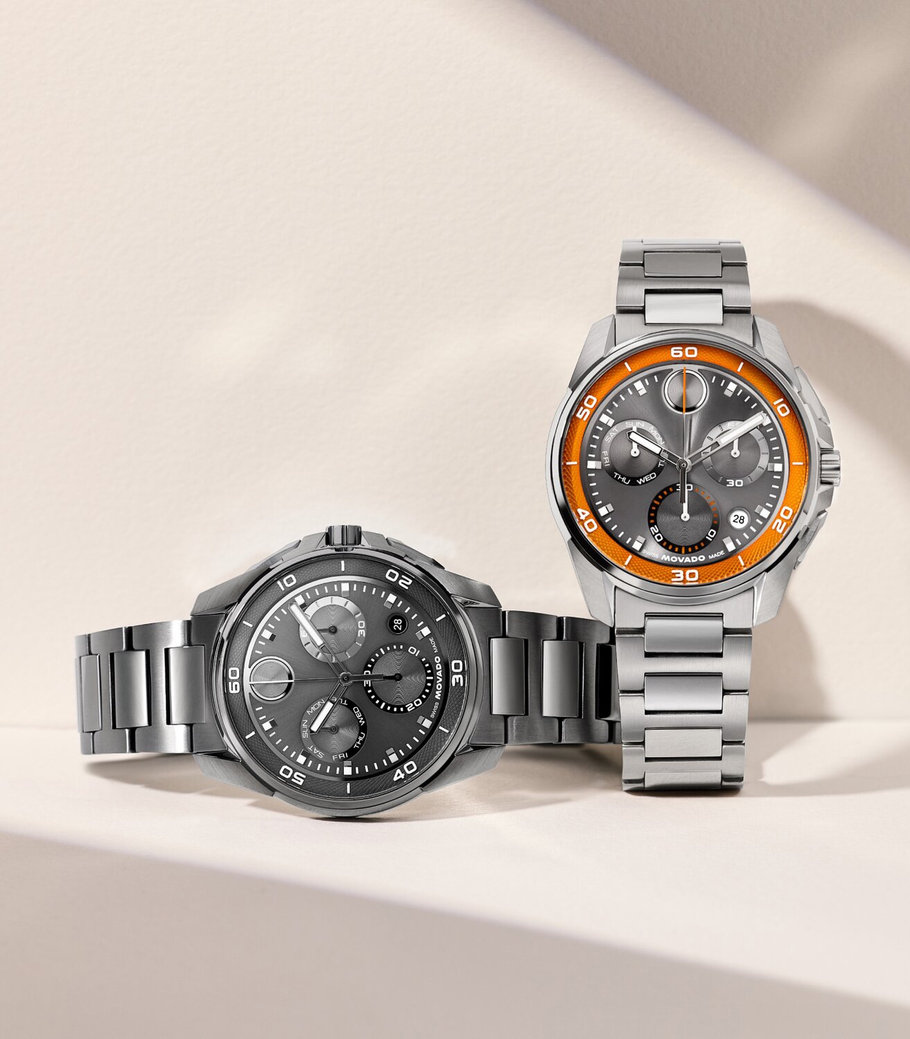 Grey plated BOLD Verso S Chronograph bracelet watch laying next to a BOLD Verso S Chronograph watch with stainless steel bracelet and grey dial with orange minute track.
