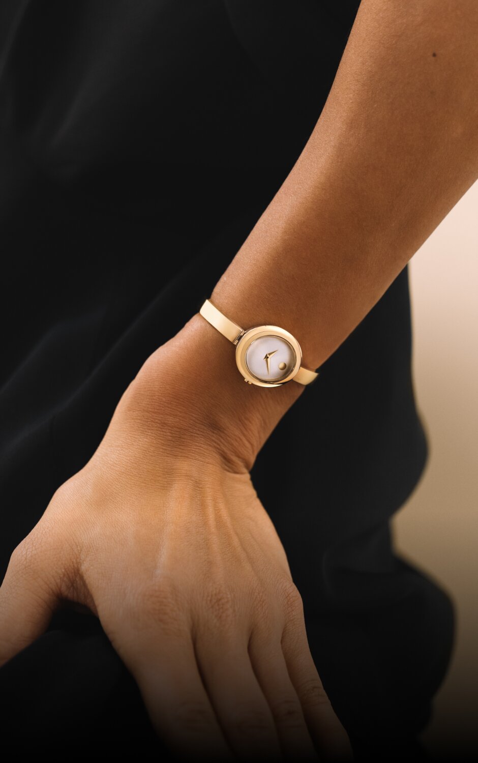 Woman in a black top wearing the gold tone Museum Bangle watch with white oval dial.
