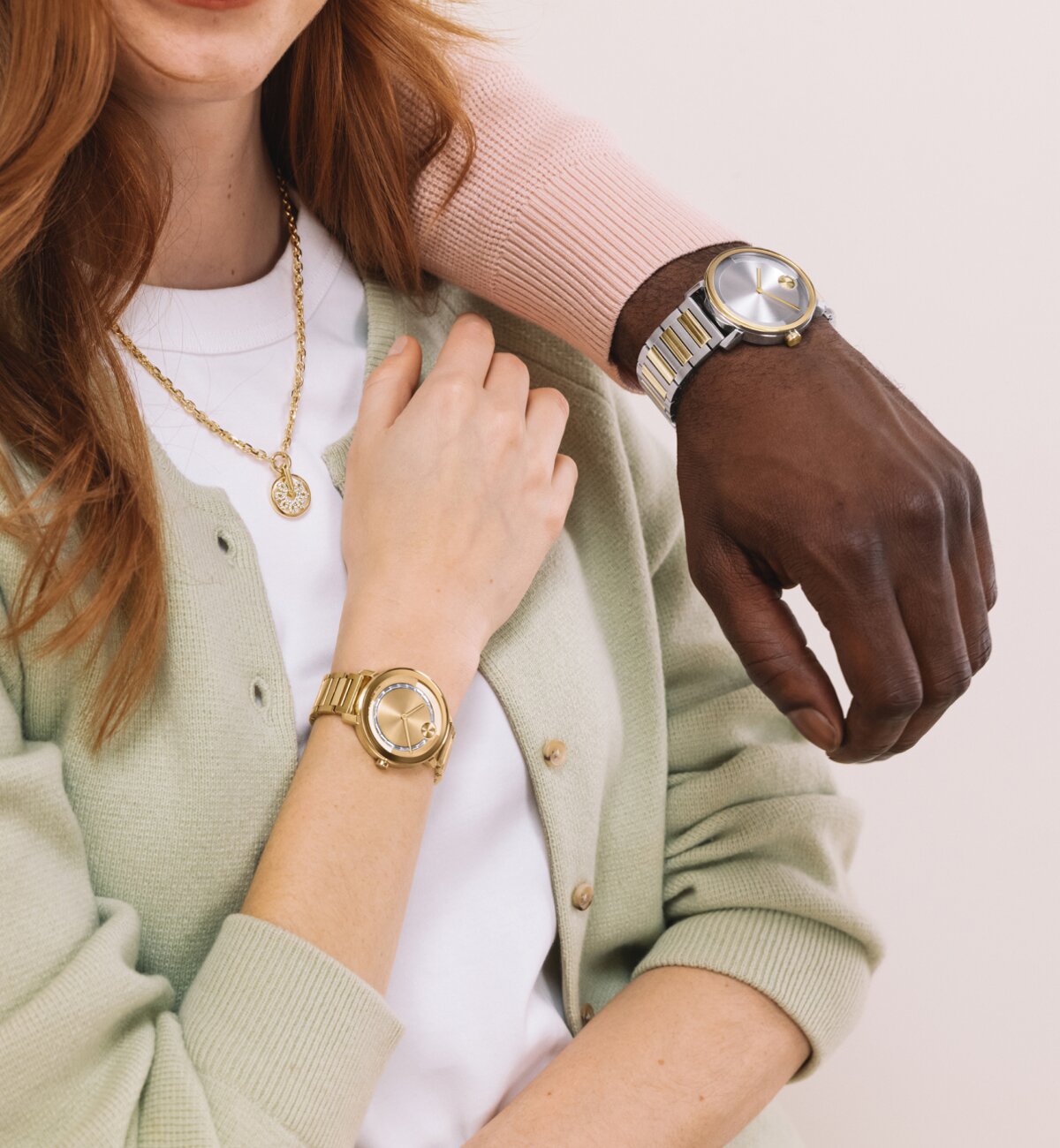 Man in a pink sweater resting his arm on a woman's shoulder while wearing a two tone BOLD Evolution 2.0 watch. The woman is wearing a green cardigan, the gold tone fleur necklace with lab grab down diamonds, and a gold tone BOLD Evolution 2.0 watch with baguette crystals on the dial. 