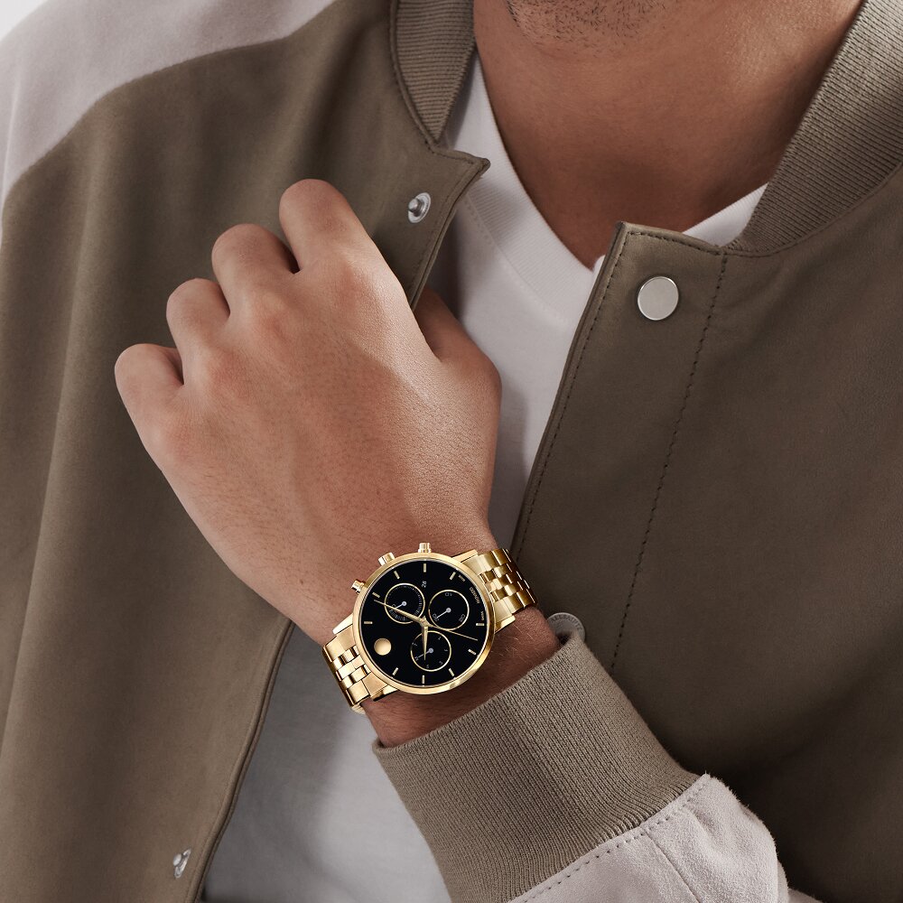 Man in a green jacket wearing the Museum Classic watch with gold tone bracelet and black chronograph dial.