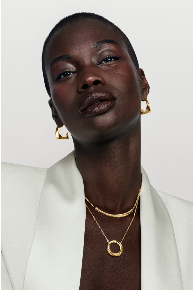 Woman in a white blazer wearing gold tone Curve earrings and two necklaces.