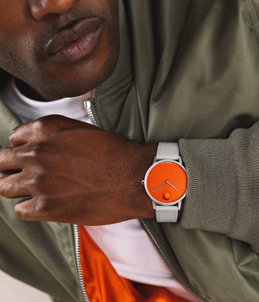 Man in a green jacket wearing the Movado Face watch with grey strap and orange dial.