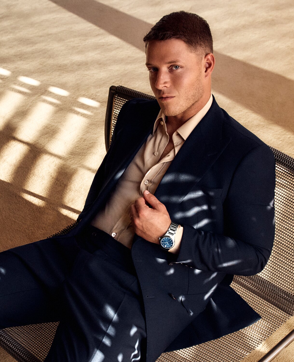 Christian McCaffrey sitting down in a suit wearing a Museum Imperiale watch with blue dial and silver bracelet.