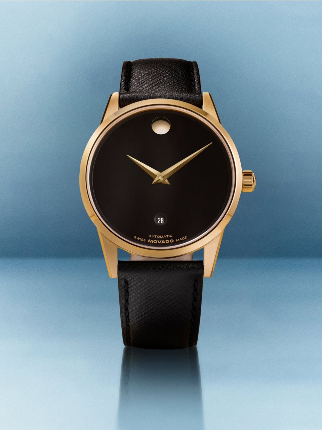 Museum Classic Automatic watch with black leather strap and black dial with gold tone accents in front of a blue background.