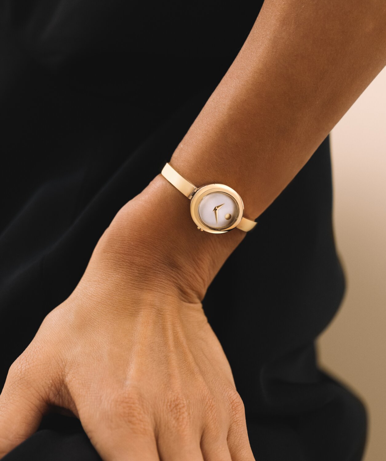 Woman in a black top wearing the gold tone Museum Bangle watch with white oval dial.