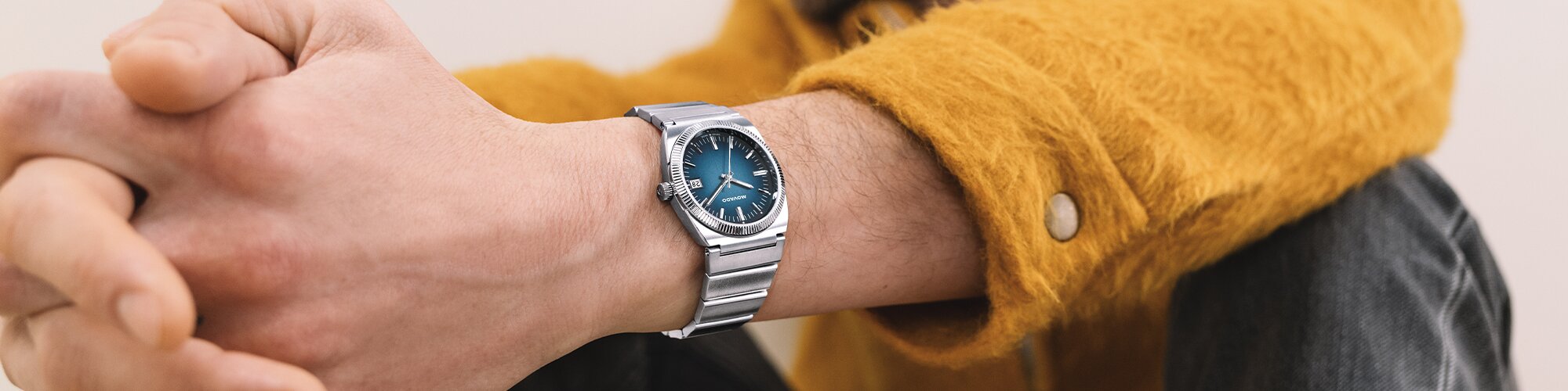 Man in an orange jacket wearing a Movado Heritage Series Ondpolan watch with silver bracelet and blue dial