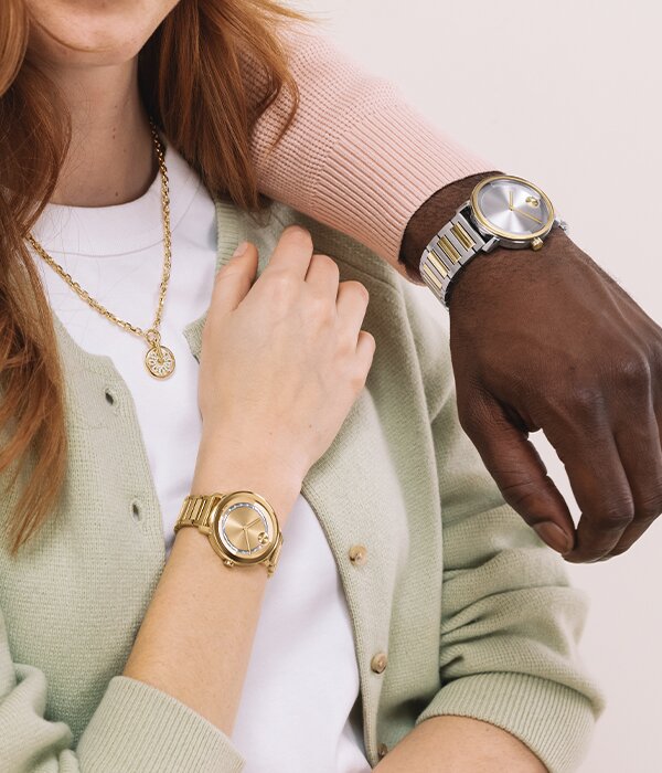 Man in a two tone Movado BOLD Evolution 2.0 watch draped over a woman wearing a gold tone fleur necklace featuring lab grown diamonds and a gold tone BOLD Evolution 2.0 watch featuring crystals.