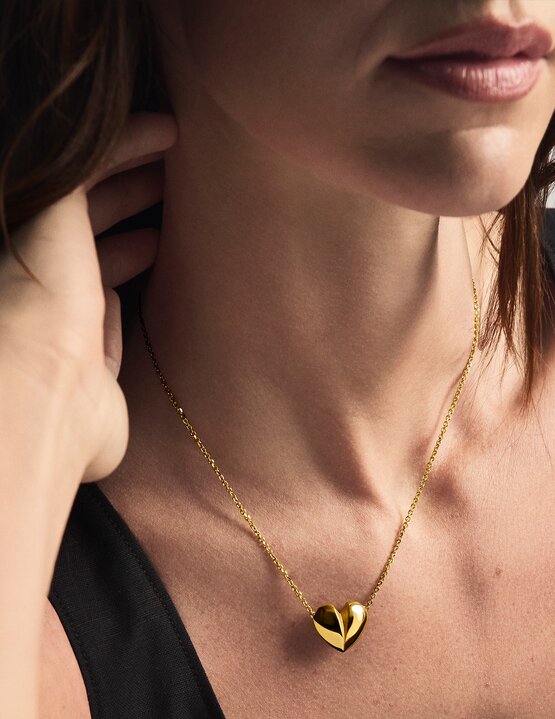 Woman wearing a gold tone heart necklace.