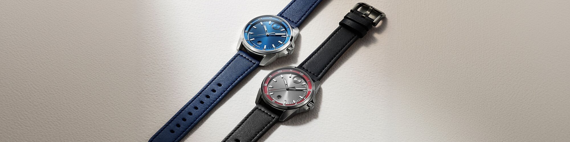 Bold Verso S watch with blue leather strap and dial laying next to a BOLD Verso S watch with black leather strap, grey dial and red hour track.