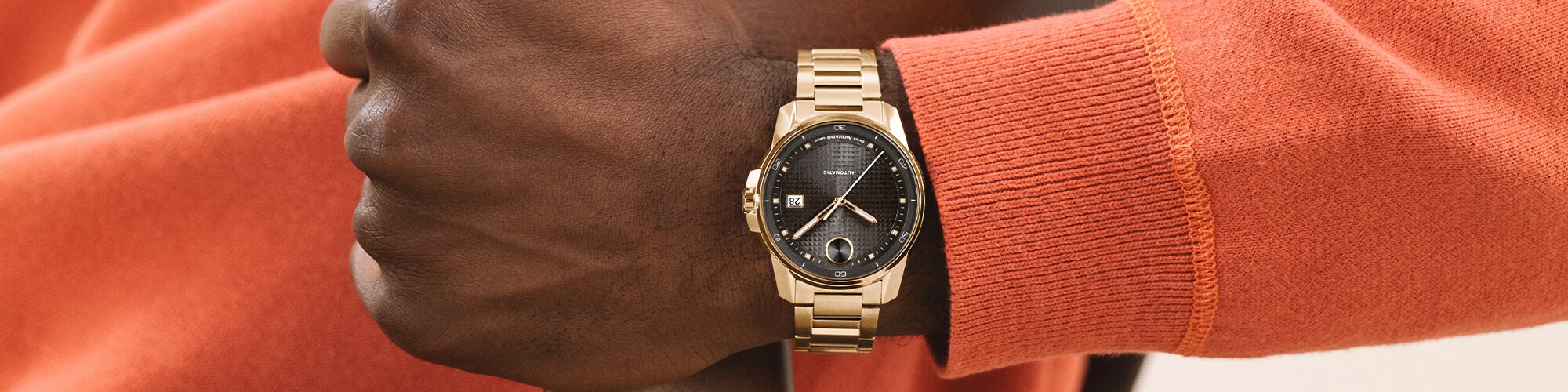 Man in an orange sweater wearing the BOLD Verso Automatic watch with gold tone bracelet and grey dial on his wrist.