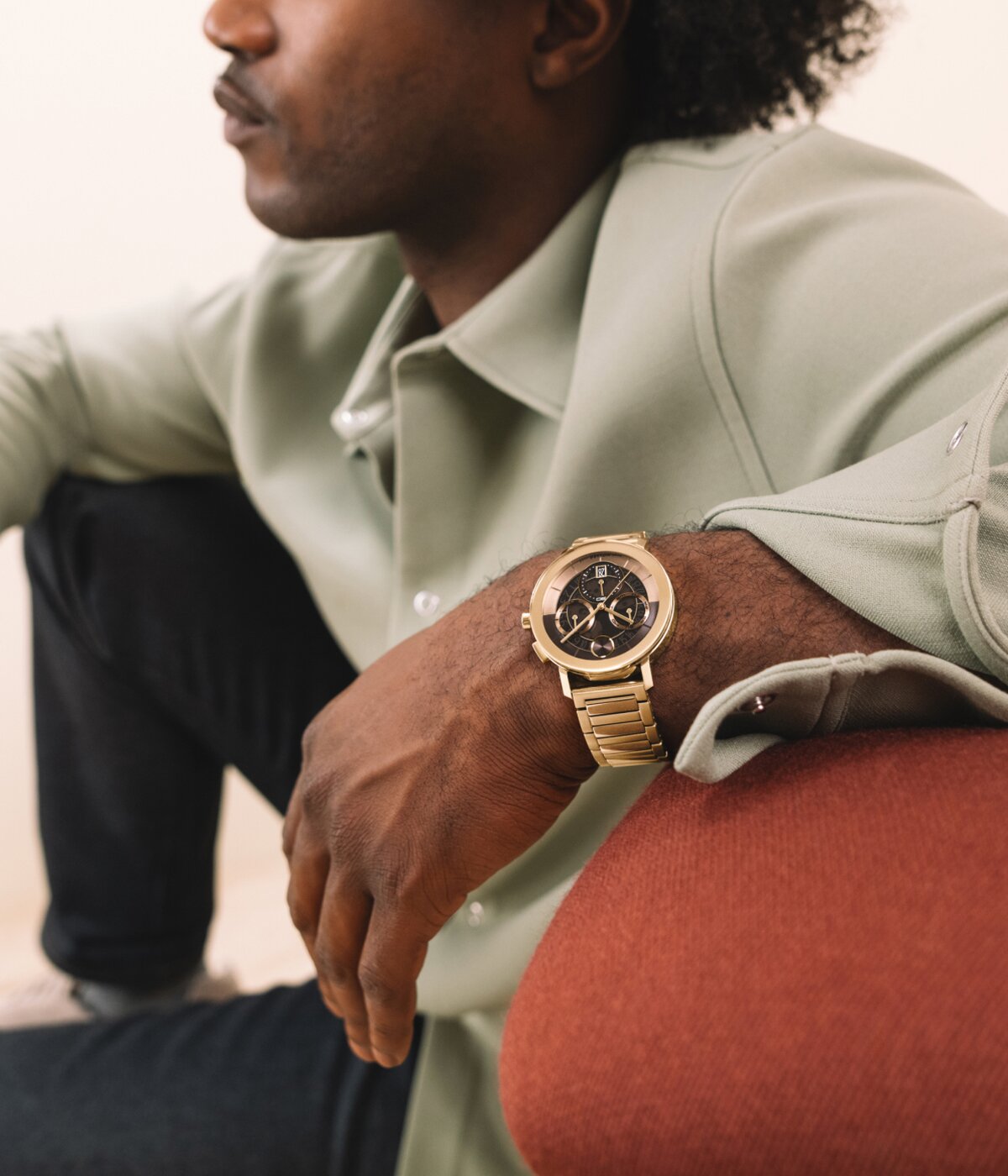 Man leaning on a sofa wearing a BOLD Evolution 2.0 watch with gold tone bracelet and brown skeleton dial.