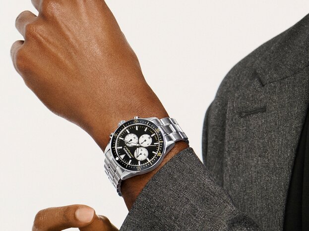 Man in a grey coat wearing the Heritage Calendoplan S watch with stainless steel bracelet and black chronograph dial.