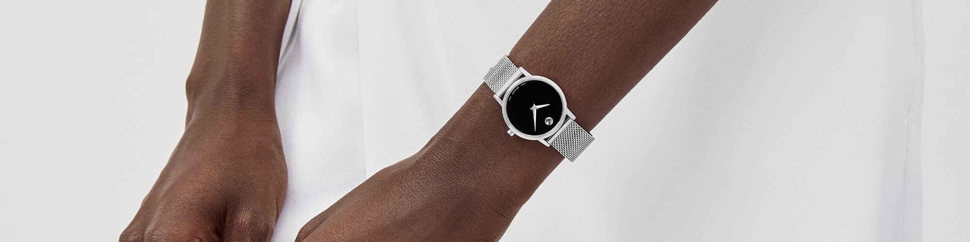 Woman in a white dress wearing a Museum classic watch with silver mesh strap and black dial