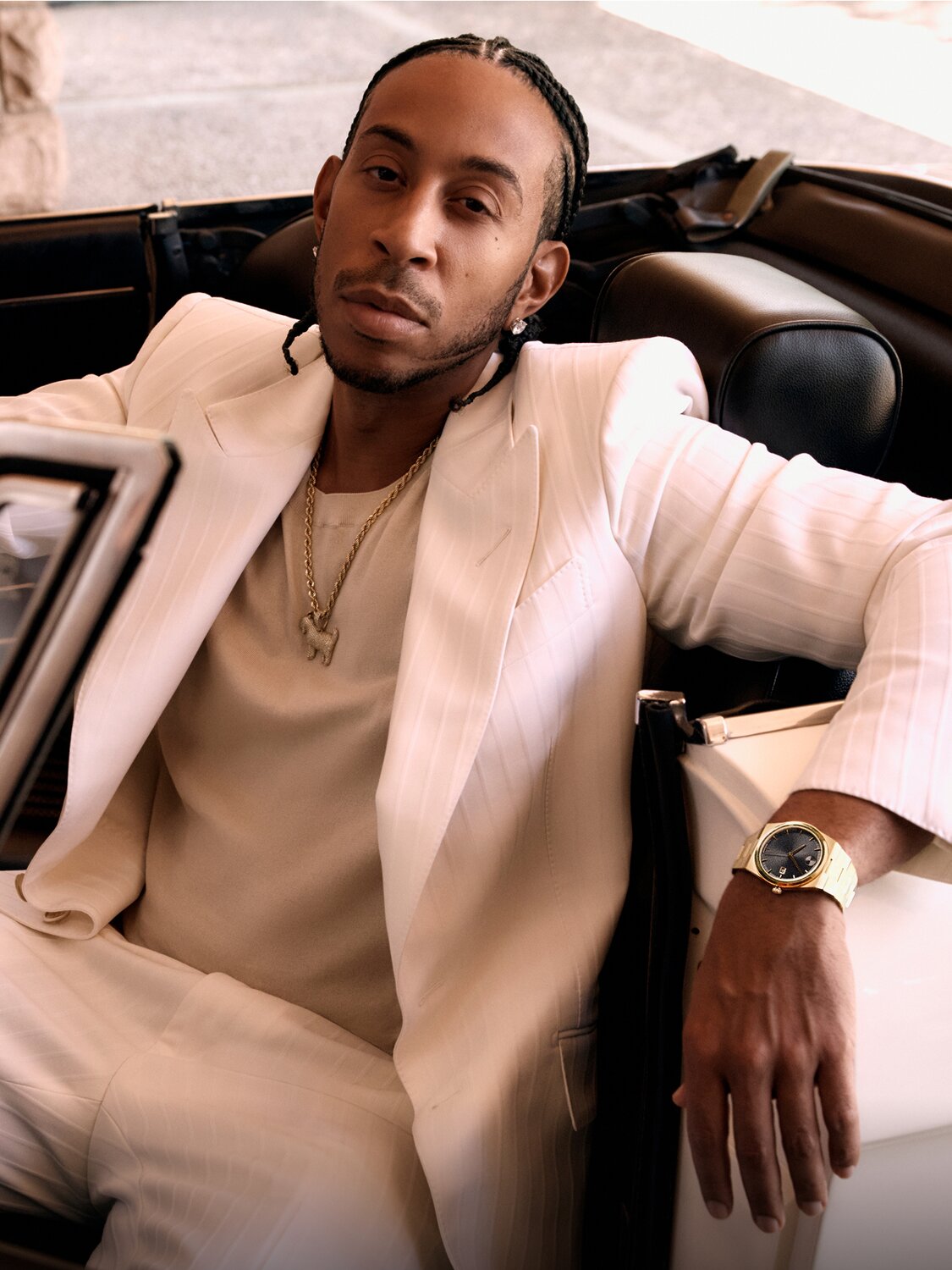 Ludacris sitting in a white car with the top down. Wearing a white suit and the BOLD Quest watch with gold tone bracelet and black dial.