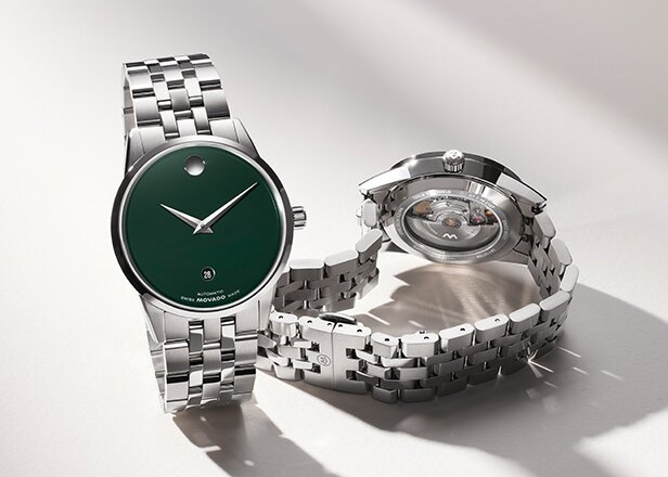 Front of a Museum Classic silver bracelet  watch with green dial behind the back of the watch with a transparent case back that showcases the automatic movement