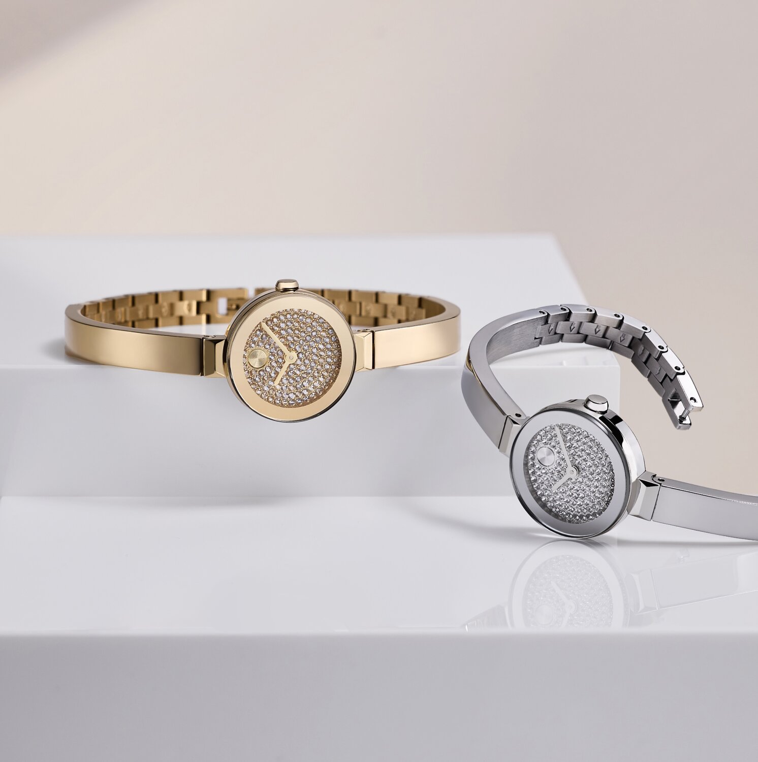 Stainless Steel BOLD Bangle Mini watch with crystal dial laying in front of a gold tone BOLD Bangle Mini watch with crystal dial.