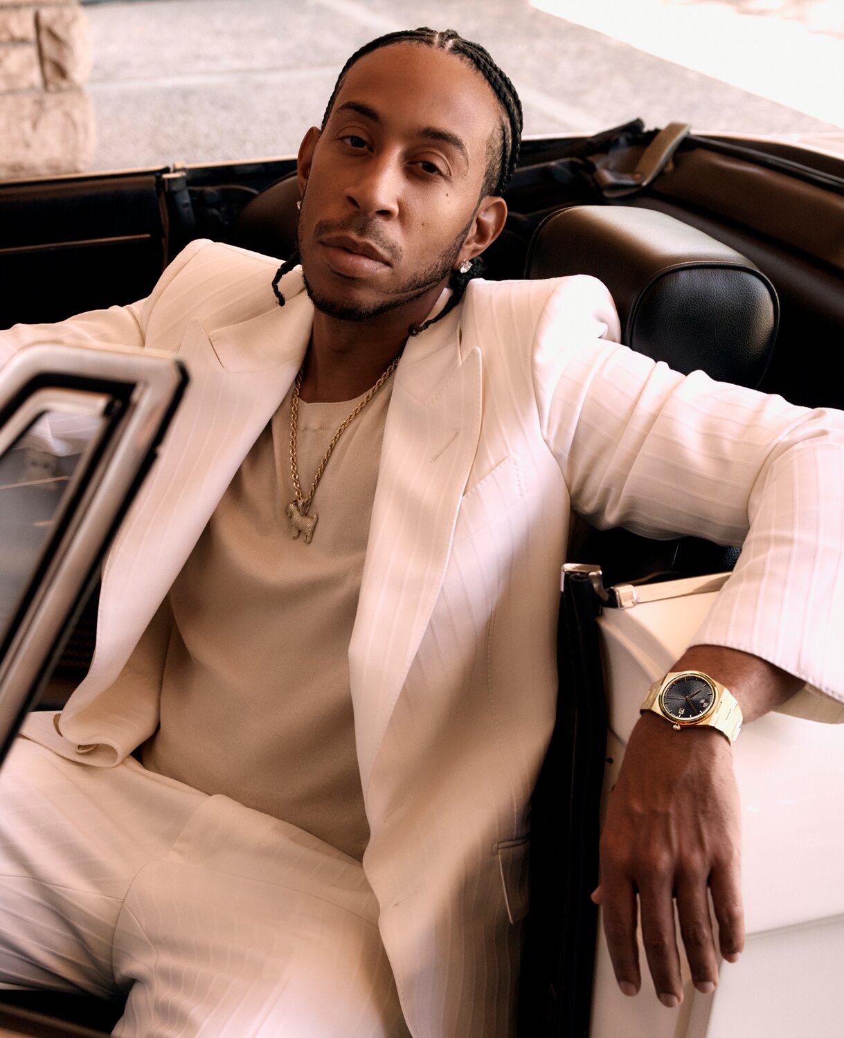 Ludacris wearing a white suit, sitting in a car, wearing the BOLD Quest watch with gold tone bracelet and black dial.