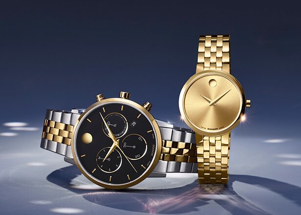 Men's two tone Museum Classic bracelet watch with black chronograph dial laying next to a gold tone Museum Classic women's bracelet watch.