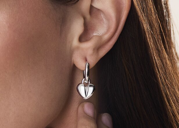 Silver sculpted heart charm earring on a woman's ear.