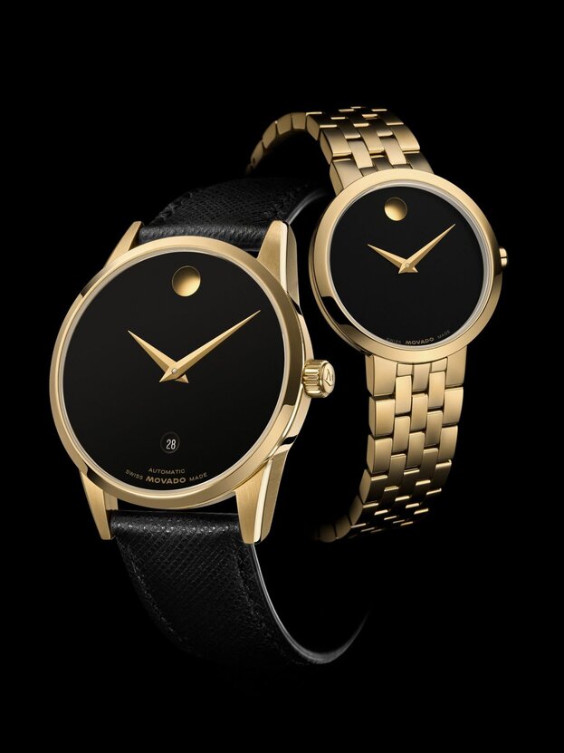 Black 40mm Museum Classic watch with leather strap and gold accents in front of a 28mm Museum Classic watch with gold tone bracelet and black dial.