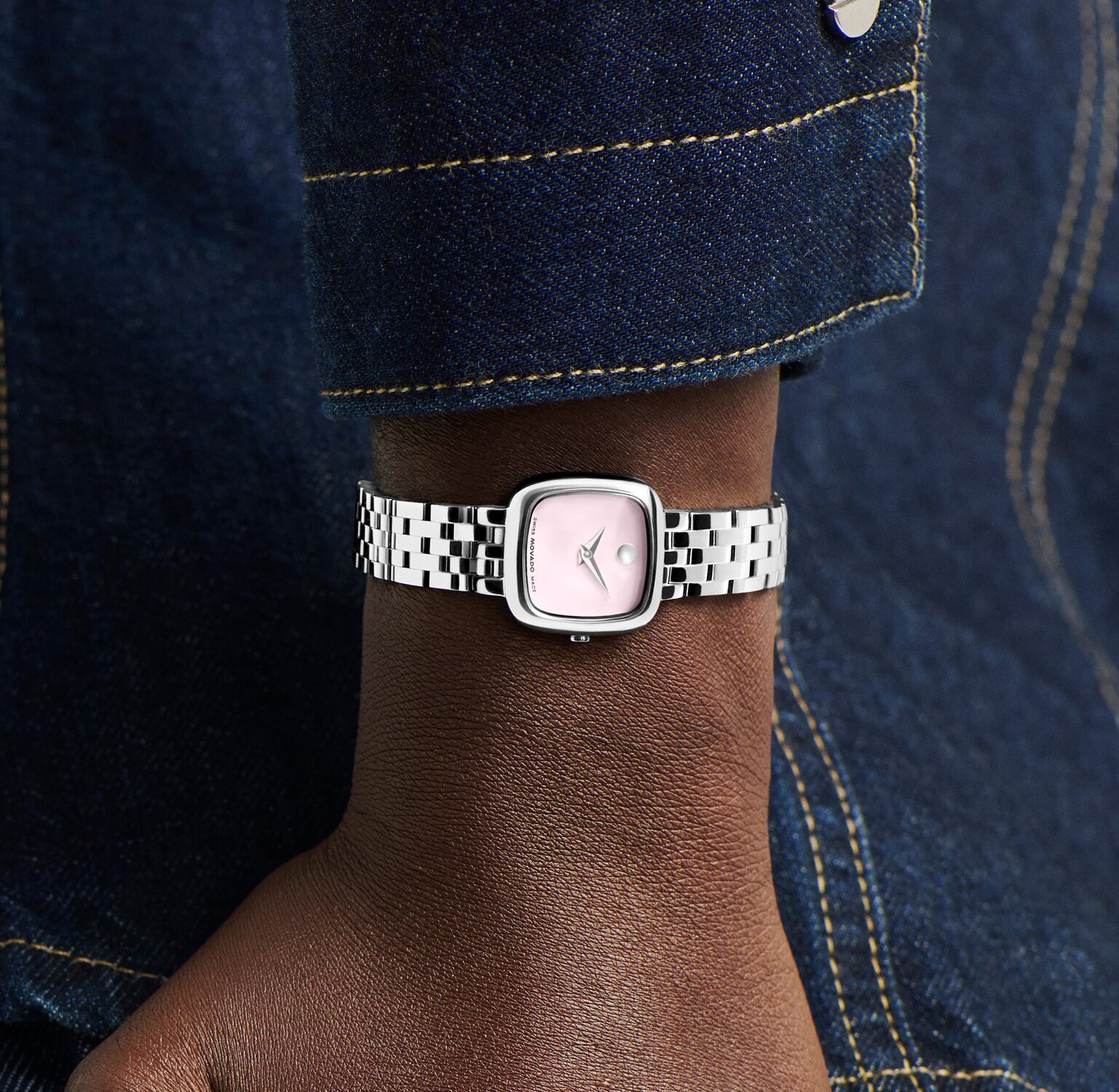 Woman in a denim jacket wearing a stainless steel Museum Classic bracelet watch with pink square dial.
