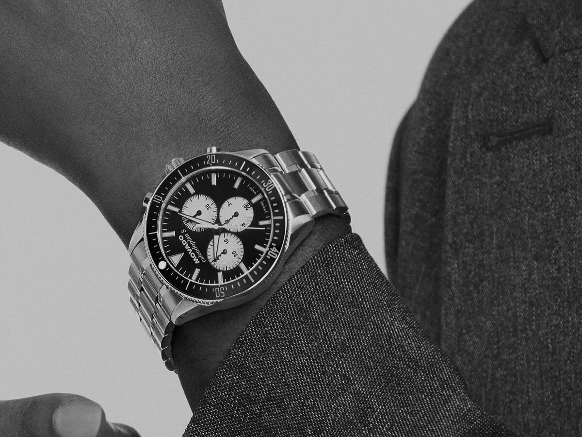 Man in a grey coat wearing the Heritage Calendoplan S watch with stainless steel bracelet and black chronograph dial.
